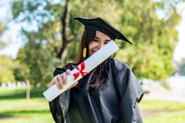 Uzun kahverengi saçlı, diplomasını gösteren mutlu bir Kafkas mezunu kız. Bekar elbisesi ve siyah bir havan topu giyiyor..