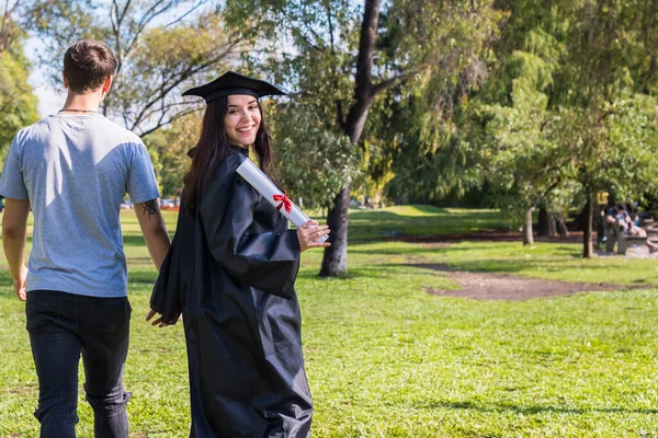 卒業証書を見せるために振り向いている間 ハッピー卒業生の女の子はボーイフレンドと手を取り合って白い歩く スペースのコピー — ストック写真