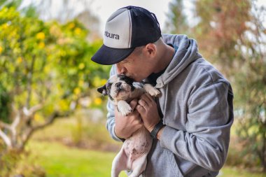 Yakışıklı bir adam sevimli bir buldog köpeğine sarılıp öpüyor. Boşluğu kopyala