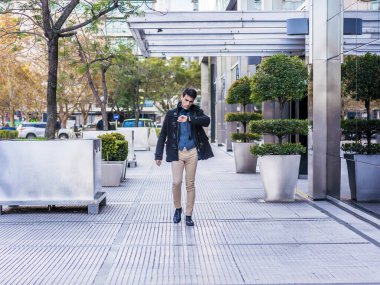 İş adamı ofisinin yanında yürürken saatine bakıyor.