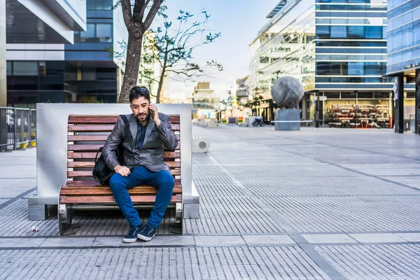 Bir iş adamı sokakta bankta otururken telefonla konuşuyor..