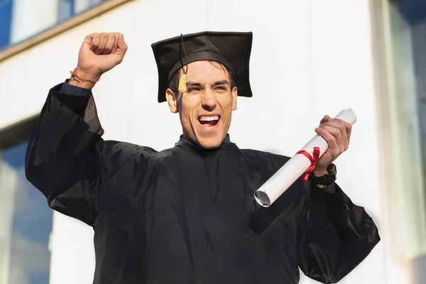 Jovem Feliz Vestindo Robe Formatura Segurando Diploma Enquanto Levanta Braço — Fotografia de Stock
