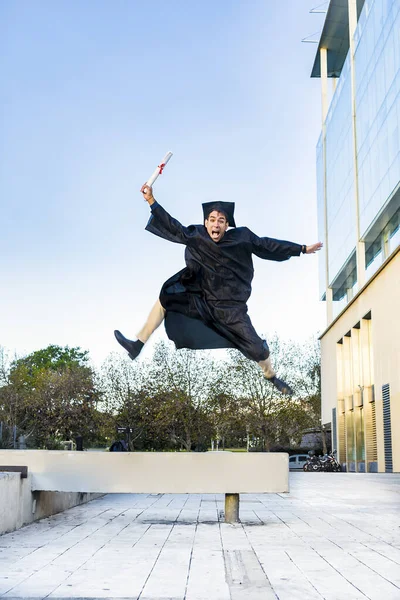Happy Graduated Man Black Gown Jumping While Holding His Diploma — Stock Photo, Image