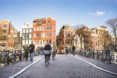Amsterdam, Hollanda - 13 Mart 2023: Amsterdam eski kentinde insanlar bisiklet sürüyor ve su kanalında yürüyorlar