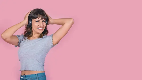 Kulaklıklı mutlu kadın pembe arka planda izole edilmiş müzik dinliyor. Stüdyo çekimi. Boşluğu kopyala