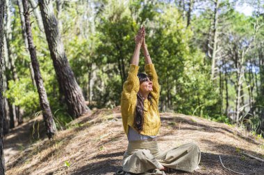 Ormanda elleri gökyüzüne yapışık meditasyon yapan bir kadın.