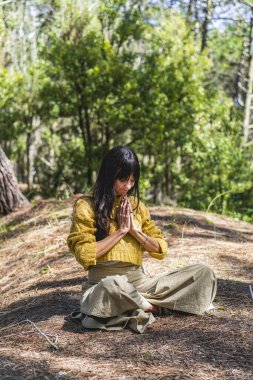 Elleri sımsıkı bağlı bir kadın ormanda meditasyon yapıyor. Dikey Çekim
