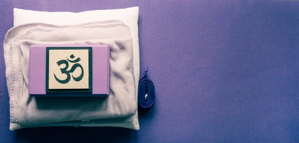 High angle view of yoga equipment. Yoga mat, block, strap, blanket, and pillow. Om sign. Copy space