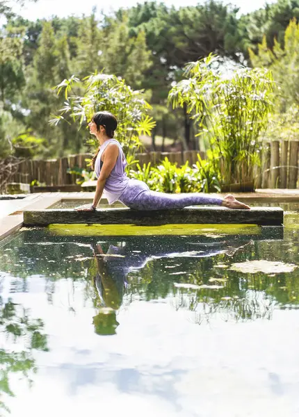 Woman practicing yoga, lying in Cobra pose (Bhujangasana exercise) outdoors. Vertical shot.