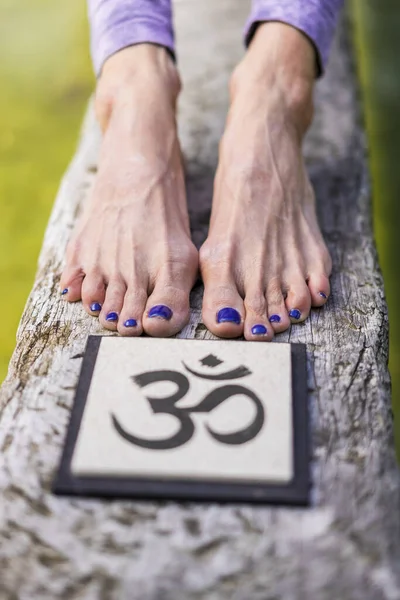 Close up of woman\'s feet behind an Om sign on a tree trunk over the water.