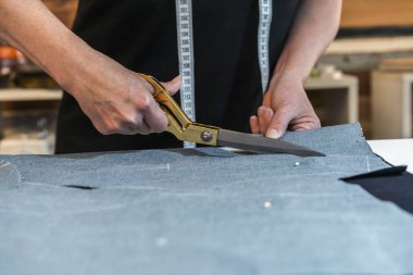 Terzi, iş masasında tekstil kesmek için makas kullanıyor..