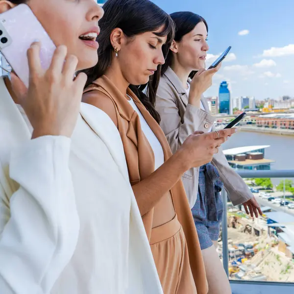 Üç kadın bir balkonda duruyor, her biri cep telefonu tutuyor. Hepsi iş kıyafetleri giymişler ve sahne, yoğun bir günde bir anı işaret ediyor.