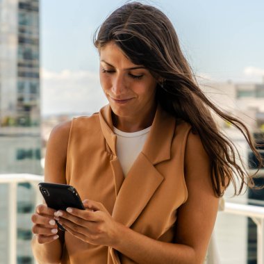 Bir iş kadını cep telefonuna mesaj yazarken gülümsüyor.