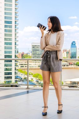 Bir kadın, bir balkonda şehre tepeden bakarken cep telefonuna mesaj bırakıyor.