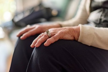 Yaşlı bir kadın, elleri dizlerinin üzerinde, sol elinde yüzükle kanepede oturuyor. Yalnızlık ve eski moda konsept