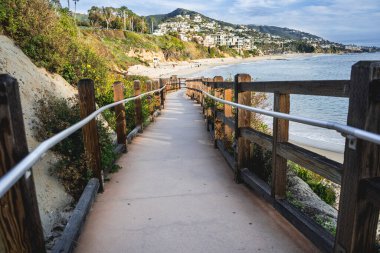 Tahta bir sahil yolu sahile çıkar. Tahta kaldırımda korkuluk var. Kumsal güzel, sakin bir yerdir. Arka planda okyanus vardır.