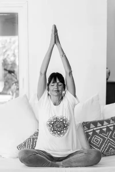 Yetişkin bir kadın gündüzleri evdeki kanepesinde meditasyon yapıyor. Doğal ışık ve avuçlarını başının üstüne bastırıyor..