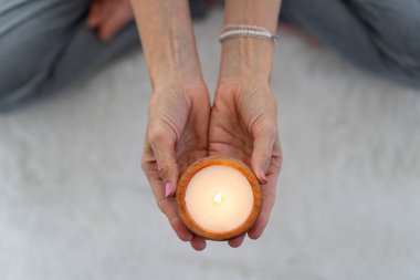 Meditasyon yapan bir kadının tuttuğu yanan bir mumun üst açısı.