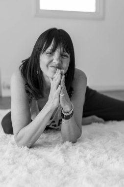 Kameraya gülümserken yoga stüdyosundaki tüylü beyaz halıda dinlenen orta yaşlı bir kadının neşeli portresi..