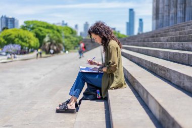 Düşünceli kadın kolejinin basamaklarında çizim yapıyor.