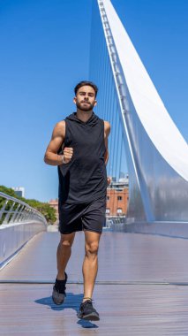 Aktif genç bir adam bir kanalın üstündeki manzaralı köprüde koşuyor.