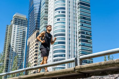 Atletik erkek modern binalarla şehir manzarasında koşuyor..