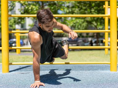 Dışarıdaki spor aletlerinde tek elle şınav çeken genç bir adam..