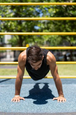 Genç adam açık hava fitness parkında şınav çekiyor..