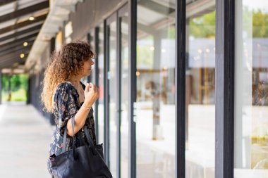 Curious woman window shopping in a modern outdoor area clipart