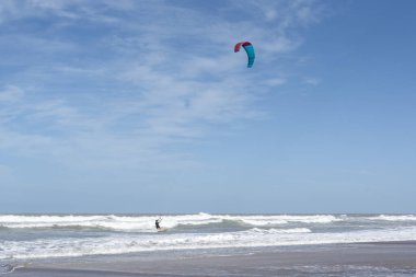 Uçurtma sörfçüsü açık mavi gökyüzünün altındaki dalgalarda geziniyor.