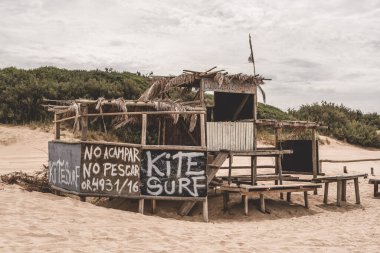Kumulların arasına gizlenmiş uçurtma sörfü tabelası olan büyüleyici bir sahil kulübesi.