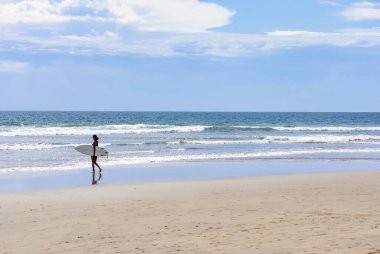 Young woman surfer walking along the beach with a surfboard on a sunny day clipart