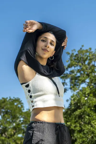 Güneşli bir şehir parkında dans eden bir kadının portresi.