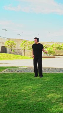 Siyah giyinmiş genç adam parkta kulaklıkla rock müzik dinlerken dans ediyor.