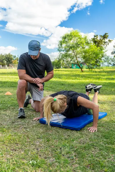 Park ayarlarında antrenörle şınav çeken bir kadının dikey çekimi.