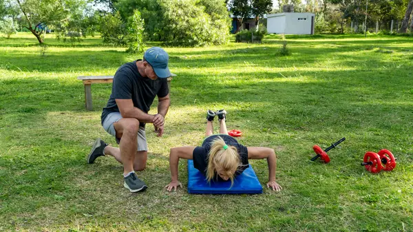 Park ortamında antrenörle şınav çeken bir kadın.