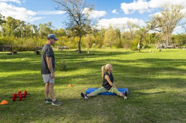 Dışarıda antrenörle esneme egzersizleri yapan bir kadın.