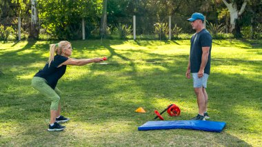 Kadın antrenörle dışarıda çömeliyor.
