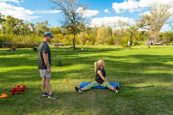 Dışarıda antrenörle esneme egzersizleri yapan bir kadın.