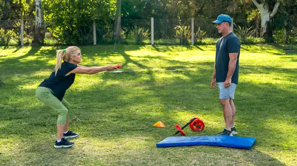 Kadın antrenörle dışarıda çömeliyor.
