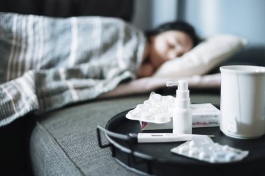 Mevsimsel soğuk algınlığından muzdarip bir kız yatakta yatıyor. Tepside antiviral ilaçlar