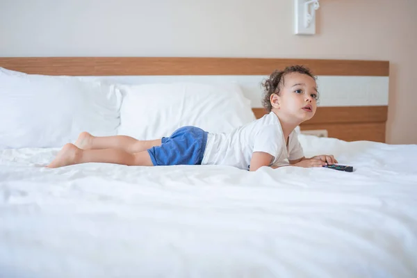 Little boy lies on his tummy on a white bed in the master bedroom