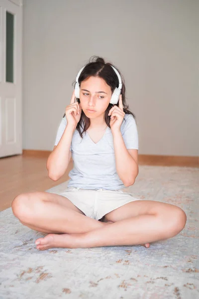 stock image Pretty young girl listening to music with headphones while by on carpet at home. Apartment living. Home life