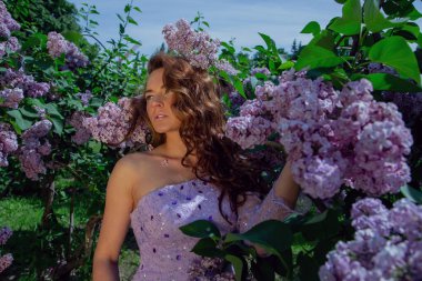 Bahar tarzı. Bahçesinde mor çalılar açan güzel elbiseli genç bir kadın. Çiçekli bahar bahçesi.