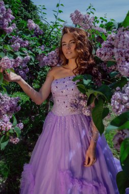 Bahar tarzı. Bahçesinde mor çalılar açan güzel elbiseli genç bir kadın. Çiçekli bahar bahçesi.