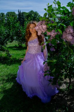 Bahar tarzı. Bahçesinde mor çalılar açan güzel elbiseli genç bir kadın. Çiçekli bahar bahçesi.