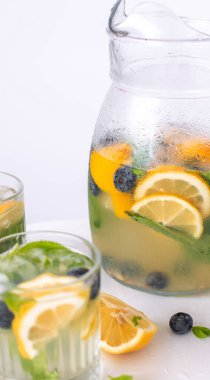 Bardakta limonata ve beyaz arka planda bir sürahi. Yaz ferahlatıcı içecek. Limonlu soğuk detoks suyu