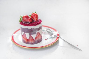 Kırmızı tabakta çilekli taze kek ve bir fincan kapuçino. Beyaz arka planda yemek ve Noel havası