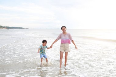 Mutlu Asyalı anne ve oğlu güneş doğarken tropikal kumsalda oynamanın keyfini çıkarıyorlar. Yaz tatilinde mutlu bir aile..