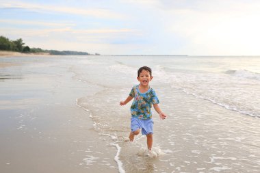 Asyalı küçük çocuk tropikal kumsalda koşuyor.